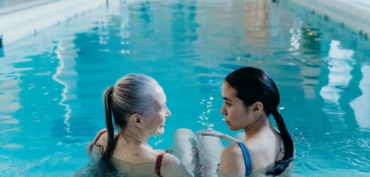 Elderly and young woman bonding in a serene indoor swimming pool environment.