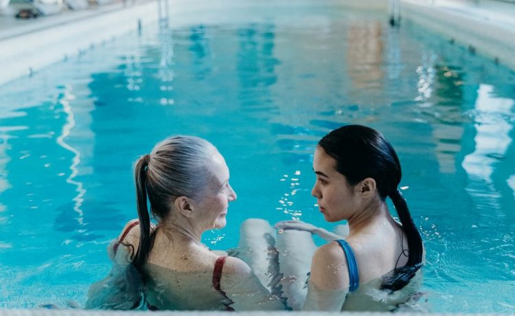 Elderly and young woman bonding in a serene indoor swimming pool environment.